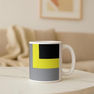 Esta imagen retrata una taza de cerámica con un diseño fuerte en negro, rojo y verde, colocada sobre una bandeja de desayuno con una tostada, en una mesa cercana a una cama y una alfombra visible. El entorno mezcla descanso y rutina, resaltando el equilibrio entre comodidad y vitalidad. Una escena cotidiana con estilo propio.