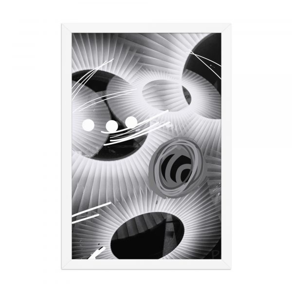 Lámina vertical en blanco y negro con formas abstractas circulares, líneas gráficas y texturas en espiral. Enmarcada en negro, tamaño real 35x40 cm, apoyada sobre mesa de madera clara junto a una lámpara negra.
